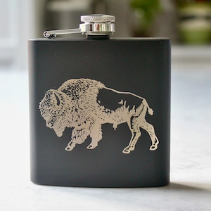 May include: Black stainless steel hip flask with a silver cap and an engraved image of a buffalo.