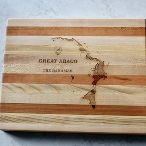 May include: A wooden chopping board with a map of Great Abaco, The Bahamas, engraved on the surface. The board is made of multiple wood types, creating a striped pattern.