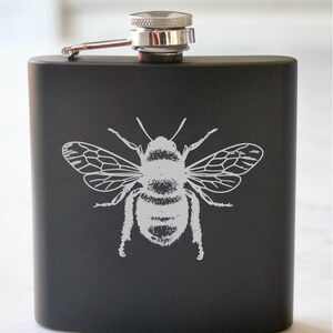 May include: Black stainless steel flask with a silver cap and a white bee design.