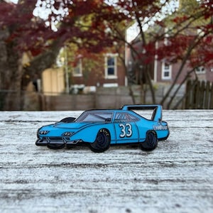 May include: A light blue race car pin with the number 33 on the side. The pin has black wheels and a rear spoiler. The word "Leadfoot" is printed on the side of the car.