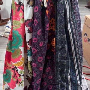 May include: A colorful, patchwork skirt with a drawstring waist. The skirt features panels of fabric with floral and paisley patterns in shades of pink, purple, white, and teal. The skirt is gathered at the waist and has a loose, flowing shape.