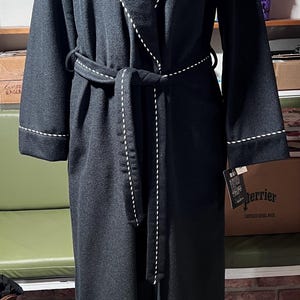 May include: A dark gray robe with white stitching along the edges and a matching belt. The robe features an embroidered emblem on the chest. The robe is displayed on a mannequin.