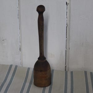 May include: A vintage wooden muddler with a rounded top and a long, slender handle. The muddler is made of dark-stained wood and has a bulbous base. It is likely used for mixing drinks or crushing ingredients.