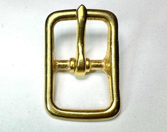 Puede incluir: Una hebilla de metal dorado de forma rectangular con una lengüeta puntiaguda. La hebilla está diseñada para usarse con correas de cuero.