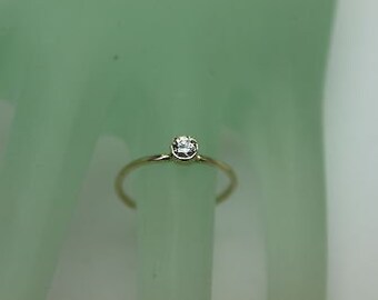 Könnte beinhalten: Ein einfacher Goldring mit einem einzigen, kleinen, runden, klaren Edelstein.