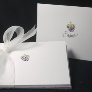 May include: White stationery set with a purple and green grape illustration. The set is tied with a sheer white ribbon. One card has the name "Emma" written in cursive.