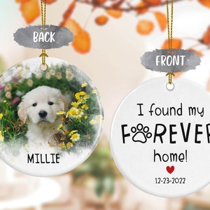 May include: A white ceramic ornament with a photo of a golden retriever puppy in a field of flowers on the back. The front of the ornament says "I found my FOREVER home!" with a paw print and a heart. The date "12-23-2022" is printed below the heart. The name "Millie" is printed on the back of the ornament.