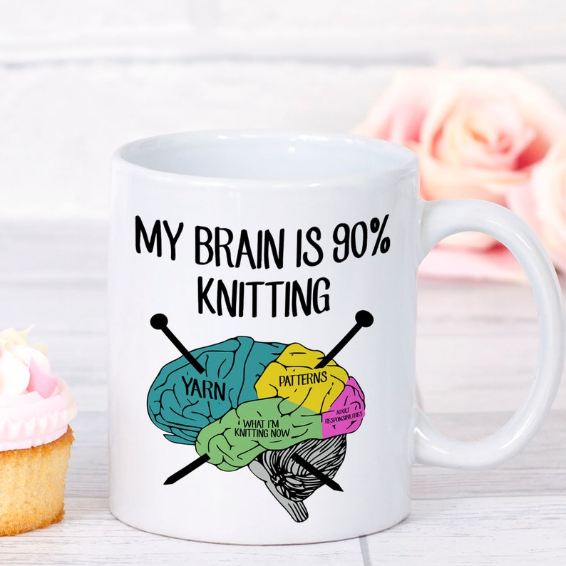May include: White ceramic mug with the text "MY BRAIN IS 90% KNITTING" and a brain graphic. The brain graphic is divided into sections labeled "YARN", "PATTERNS", "WHAT I'M KNITTING NOW", and "ADULT RESPONSIBILITIES". Two knitting needles cross the brain.