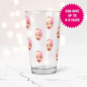 May include: A clear glass pint glass with a pattern of multiple baby faces. The glass has a white background and the faces are printed in color. The text "Can have up to 4-5 faces" is printed on a pink starburst.