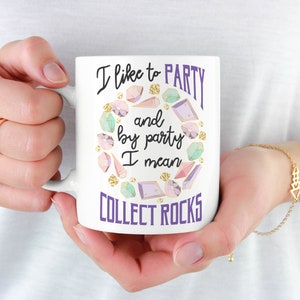 May include: White ceramic mug with a purple and gold design. The mug features the text "I like to party and by party I mean collect rocks".