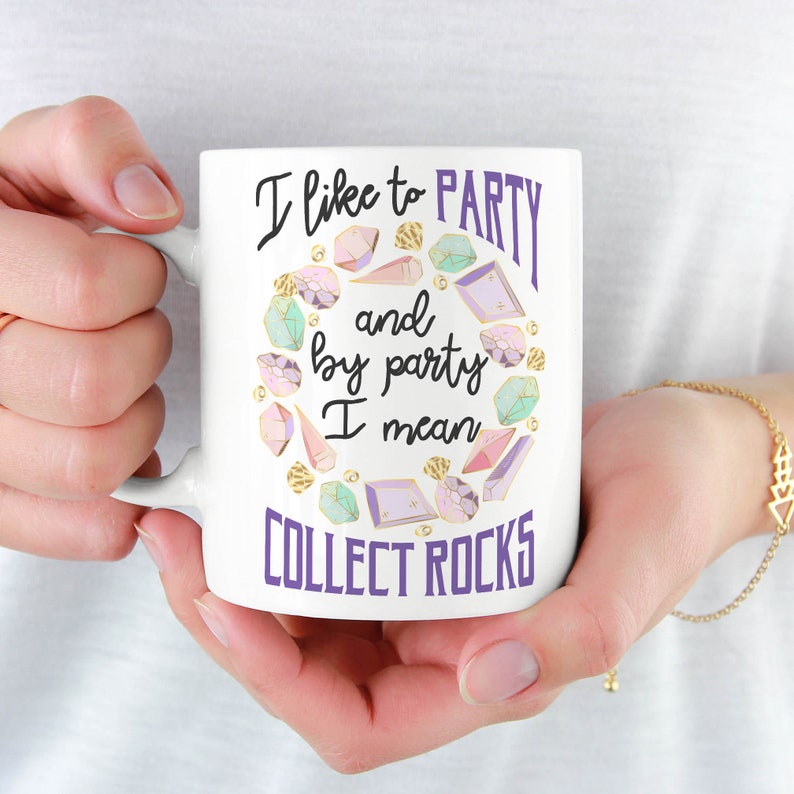 May include: White ceramic mug with a purple and gold design. The mug features the text "I like to party and by party I mean collect rocks".