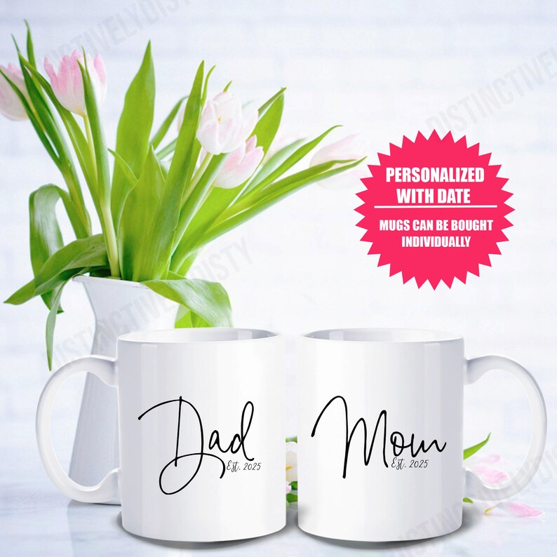 May include: Two white ceramic mugs featuring black cursive text. One mug displays the word Dad with Est. 2025 underneath, and the other displays the word Mom with Est. 2025 underneath. A pink starburst graphic includes the text Personalized with date.