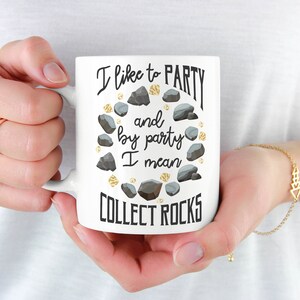 May include: White ceramic mug featuring a black and white graphic that reads "I like to party and by party I mean collect rocks". The graphic is encircled by small grey rocks and gold accents.