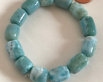 May include: A light blue gemstone bracelet with a light blue and white marbled pattern. The bracelet is made of round beads and is approximately the size of a US penny.