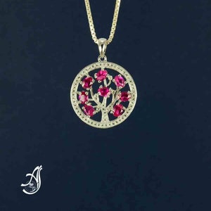 May include: A gold chain necklace with a pendant featuring a silver tree with red gemstones. The pendant is round and has a detailed design.