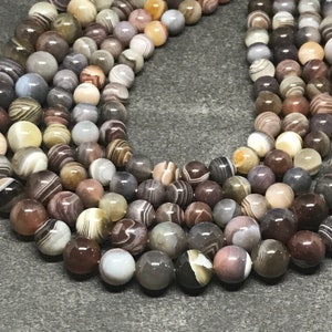 May include: A strand of brown, white, and gray agate beads. The beads are round and have a polished finish. The beads are strung on a clear elastic cord.