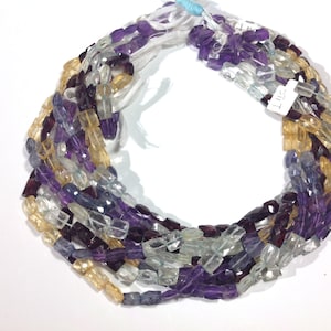 May include: A strand of faceted gemstone beads in shades of purple, blue, and yellow. The beads are arranged in a circular pattern, with the ends of the strand overlapping.