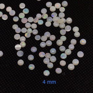 Pu&ograve; includere: Una vista ravvicinata di un mucchio di cabochon di opale bianco, ognuno con un diametro di 4 mm. Le pietre hanno un sottile bagliore iridescente.