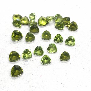 May include: A collection of 25 green peridot heart-shaped gemstones. The stones are faceted and have a light green color.