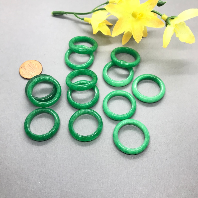 Pu&ograve; includere: Una collezione di dieci anelli di giada verde, alcuni impilati uno sopra l'altro. Gli anelli sono lisci e lucidi, e hanno un colore verde chiaro.