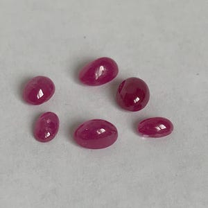Puede incluir: Seis piedras preciosas de rubí de forma ovalada en varios tamaños. Las piedras preciosas son de color rojo intenso y tienen un acabado liso y pulido.