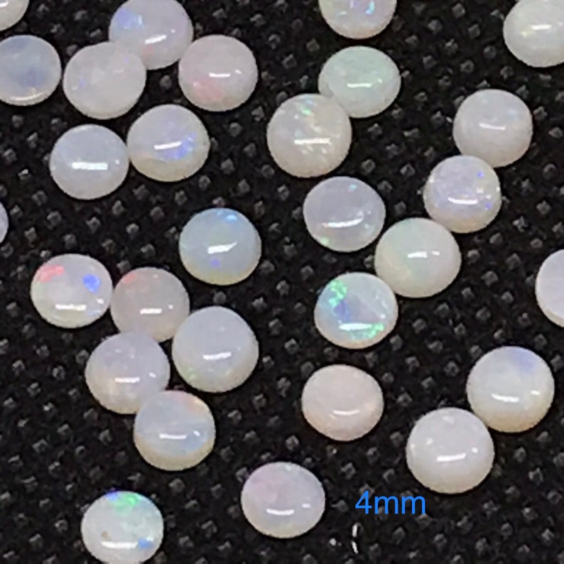 Pu&ograve; includere: Primo piano di un gruppo di cabochon di opale bianco, ognuno con un diametro di 4 mm. Gli opali hanno una sottile lucentezza iridescente.