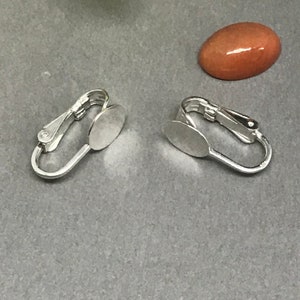 May include: Two silver earring settings with round, flat, silver-toned pads. The pads are designed to hold a cabochon stone.