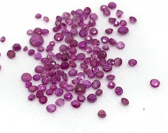 May include: A loose pile of small, round, pink gemstones. The gemstones are scattered on a white surface.
