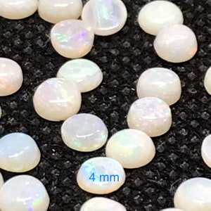Pu&ograve; includere: Primo piano di un gruppo di cabochon di opale bianco, ognuno con un diametro di 4 mm. Gli opali hanno una sottile lucentezza iridescente.