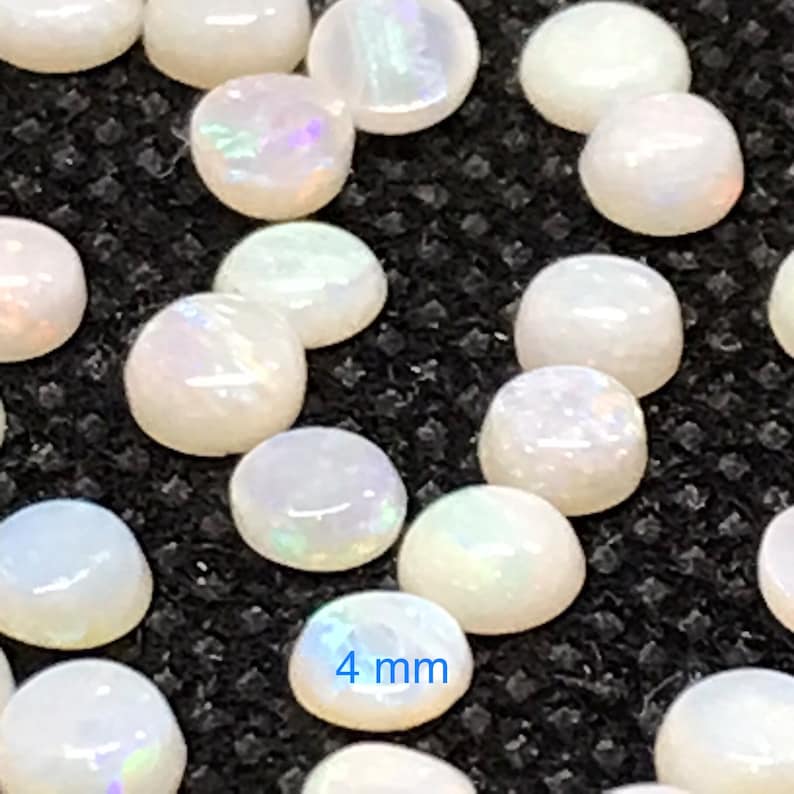 Pu&ograve; includere: Primo piano di un gruppo di cabochon di opale bianco, ognuno con un diametro di 4 mm. Gli opali hanno una sottile lucentezza iridescente.