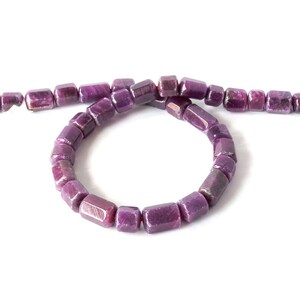 May include: A strand of deep purple, rectangular beads, possibly gemstones, arranged in a circular shape. The beads are strung on a red string, with a few beads extending in a straight line. The background is plain white.
