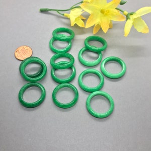 Pu&ograve; includere: Una collezione di 12 anelli in giada verde, impilati e disposti su una superficie grigia. Gli anelli sono lisci e lucidi, con un bagliore sottile.