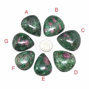 Könnte beinhalten: Sieben grüne und rosafarbene Edelstein-Cabochons, mit A bis G beschriftet, in einem Kreis um eine US-Münze angeordnet. Die Cabochons sind alle tropfenförmig und haben eine glatte, polierte Oberfläche.