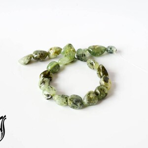 Puede incluir: Una hebra de cuentas de piedras preciosas verdes y negras, enhebradas en un cordón blanco. Las cuentas tienen una forma irregular y un acabado natural y pulido.