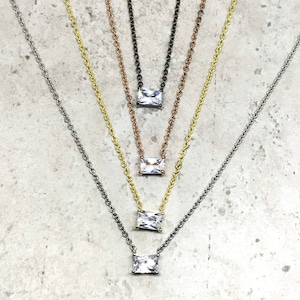 May include: Five silver, gold, and black necklaces with a square-shaped clear crystal pendant.