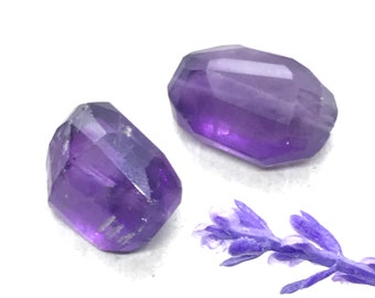 Peut inclure: Deux pierres précieuses d'améthyste facettées, l'une est violette clair et l'autre violette foncé, toutes deux sur une surface blanche avec une brindille de lavande.