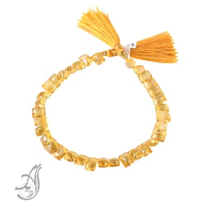 May include: A yellow gemstone bracelet with a tassel on each end. The bracelet is made of faceted, square-shaped gemstones.