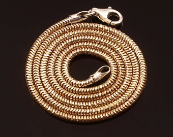 May include: A gold snake chain necklace with a silver clasp. The chain is coiled into a circle.