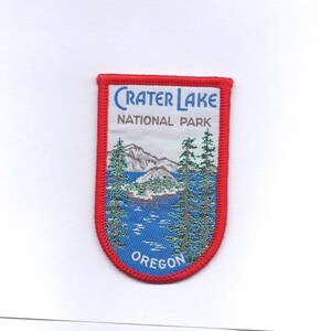 May include: A red, white, and blue embroidered patch with the text "Crater Lake National Park Oregon". The patch features a scenic image of a lake and mountains.