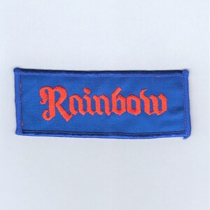 May include: A blue fabric patch with the word "Rainbow" embroidered in orange.