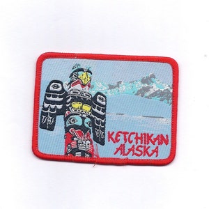 May include: Red embroidered patch with a colorful totem pole and mountains in the background. The text "KETCHIKAN ALASKA" is embroidered in red.