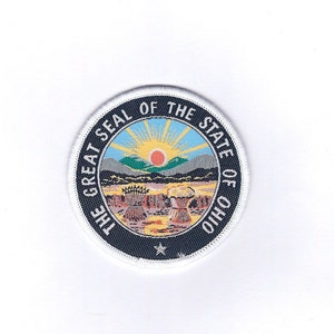 May include: A white embroidered patch with the Great Seal of the State of Ohio. The seal features a sunrise over a mountain range, a buckeye nut, and a sheaf of wheat.
