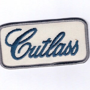May include: A white embroidered patch with a gray border. The word "Cutlass" is embroidered in blue.