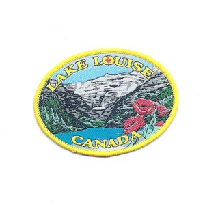 May include: A yellow oval embroidered patch with a scenic view of Lake Louise, Canada. The patch features a mountain range with snow-capped peaks, a lake, and red flowers. The text "LAKE LOUISE CANADA" is embroidered in yellow around the edge of the patch.