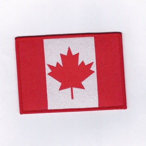 Peut inclure: Un écusson de drapeau canadien rouge et blanc avec une feuille d'érable rouge au centre.