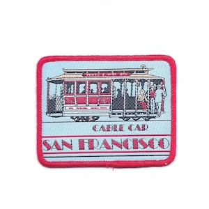 May include: Red and black cable car with passengers, a blue and red embroidered patch with the text "Cable Car San Francisco" and "Powell & Hyde St."