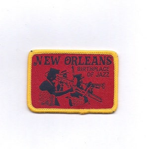 May include: A red and yellow embroidered patch with the text "NEW ORLEANS BIRTHPLACE OF JAZZ" and a black silhouette of two musicians playing instruments.