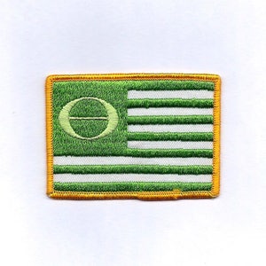 May include: Green and white embroidered patch with a yellow border. The patch features a green circle with a white letter "O" and a white horizontal line through the center of the circle. The circle is centered on the left side of the patch. The right side of the patch features seven horizontal white stripes alternating with seven horizontal green stripes.