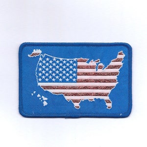 May include: A blue fabric patch with an embroidered outline of the United States of America. The outline is filled with the American flag, with red and white stripes and white stars on a blue field.