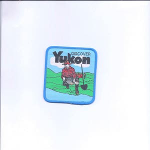 May include: A blue and white embroidered patch with the text "DISCOVER YUKON" and a cartoon image of a person panning for gold.